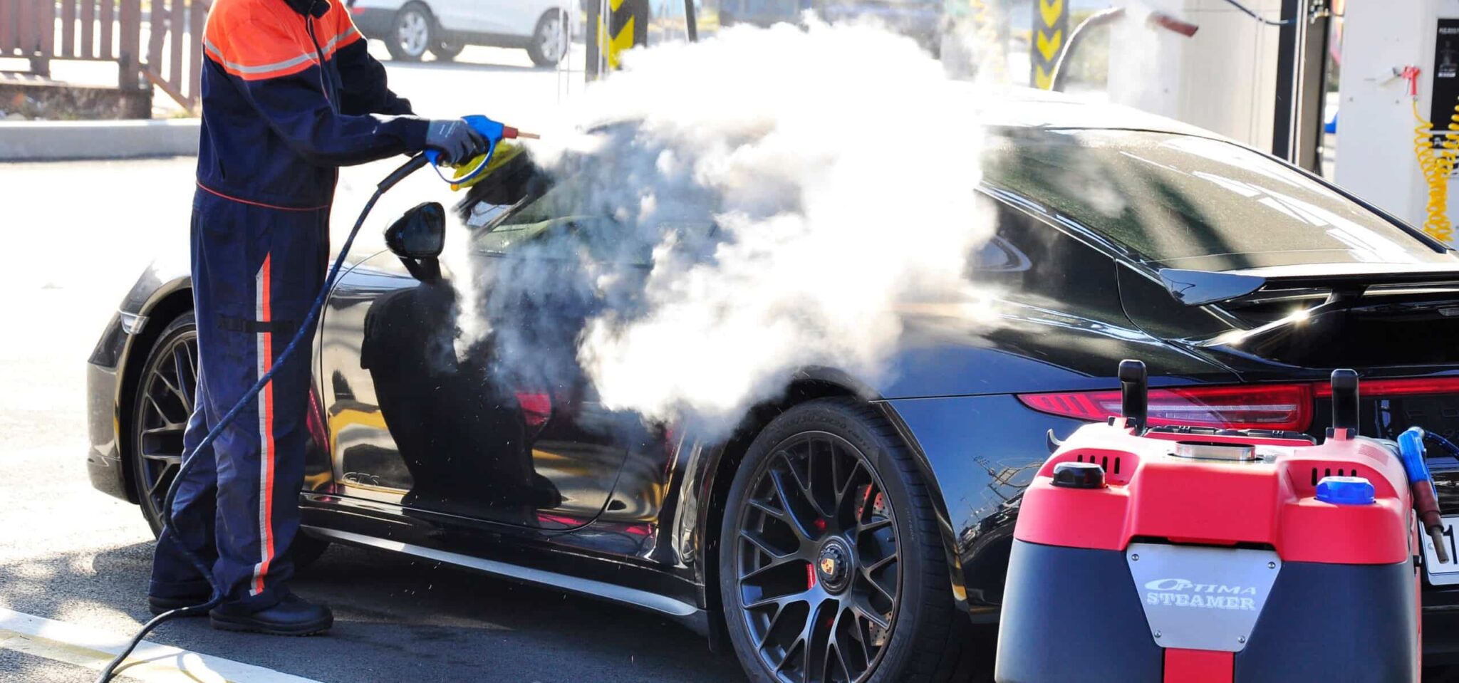 Mobile car wash operator steam cleaning the exterior of a black sports car using the Optima XD Steamer
