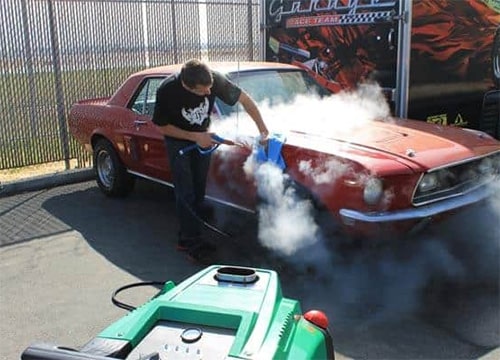 Person using an Optima DMF Steamer and microfiber cloth to clean the exterior of a vintage red car